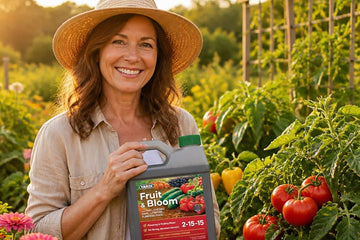Woman holding a bottle of YARDi Fruit & Bloom liquid fertilizer in a garden with tomatoes and flowers.